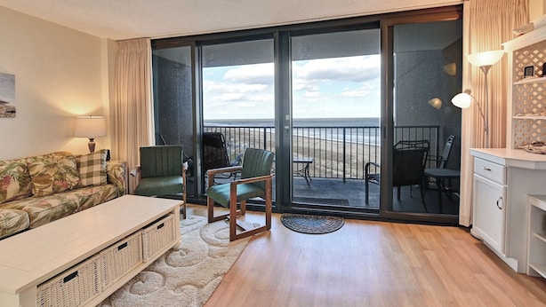 Een gezellige woonkamer met een bank, fauteuils, een bijzettafeltje en uitzicht op het strand door grote glazen schuifdeuren.