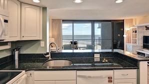 Een keuken met uitzicht op zee, een spoelbak en een eethoek met stoelen.
