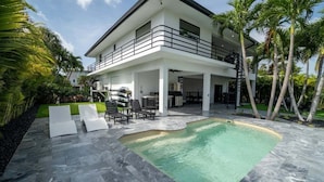 Une maison moderne à deux étages dotée d’une piscine, d’un espace salon extérieur et d’un balcon.