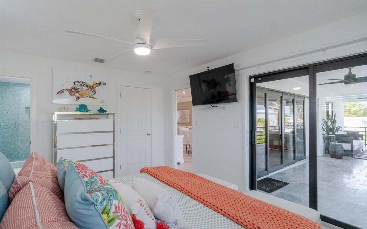 Quarto moderno com cama, TV e porta de vidro deslizante que dá para um pátio.