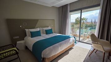 A hotel room with a large bed, a chair, a small table, and a view of a pool and palm trees.