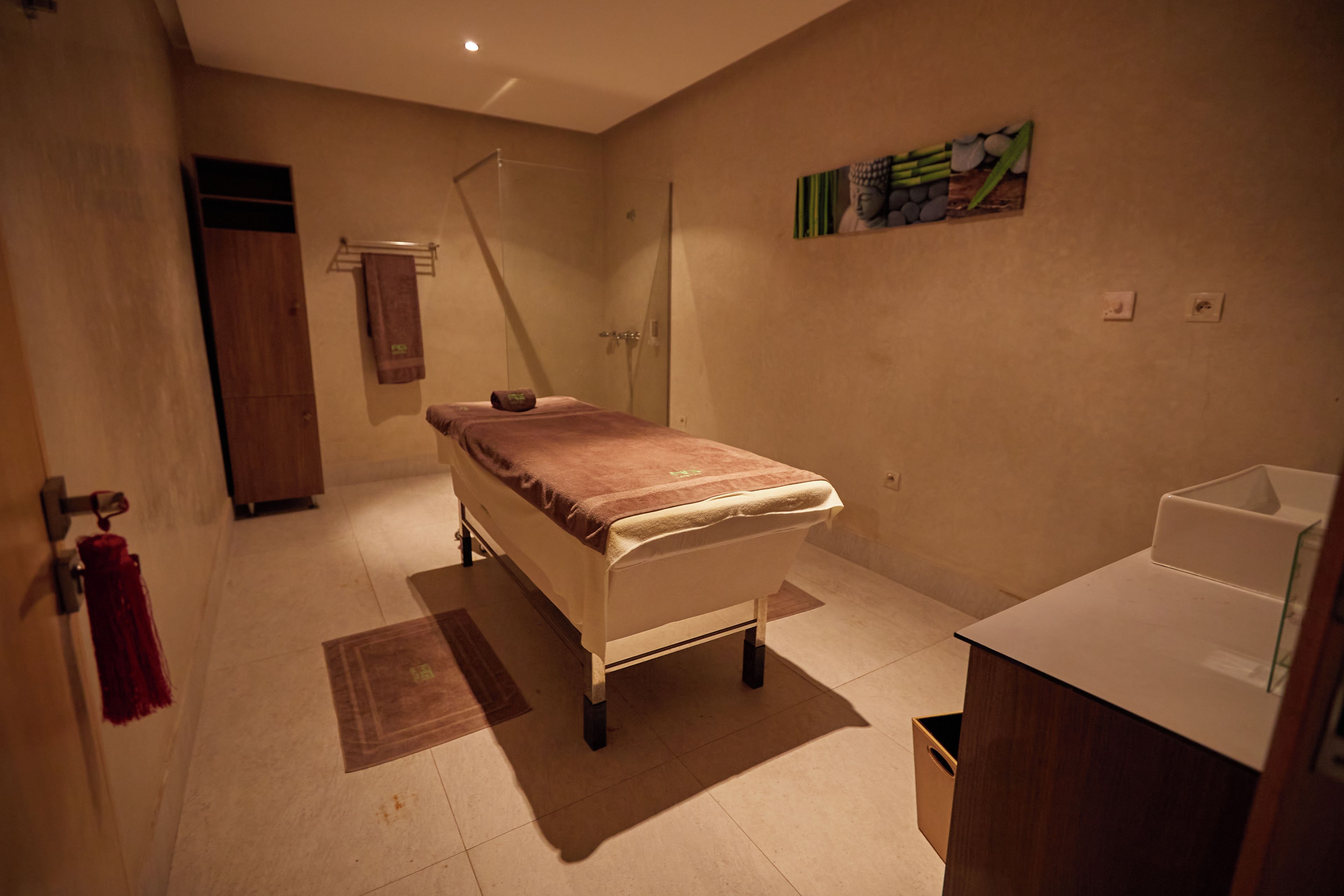 A room with a bed, a small bedside table, a shower, and a wall-mounted artwork.