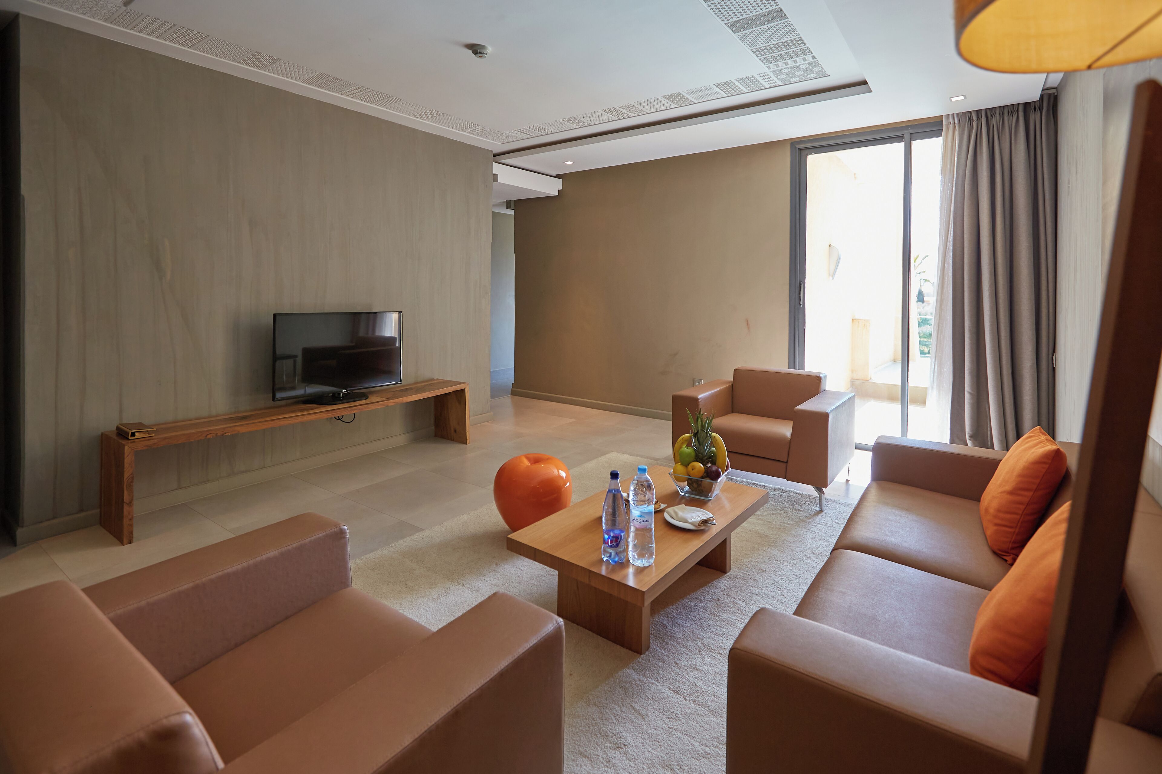 A modern living room with a sofa, a coffee table with water bottles, a fruit bowl, and a television on a wooden stand.
