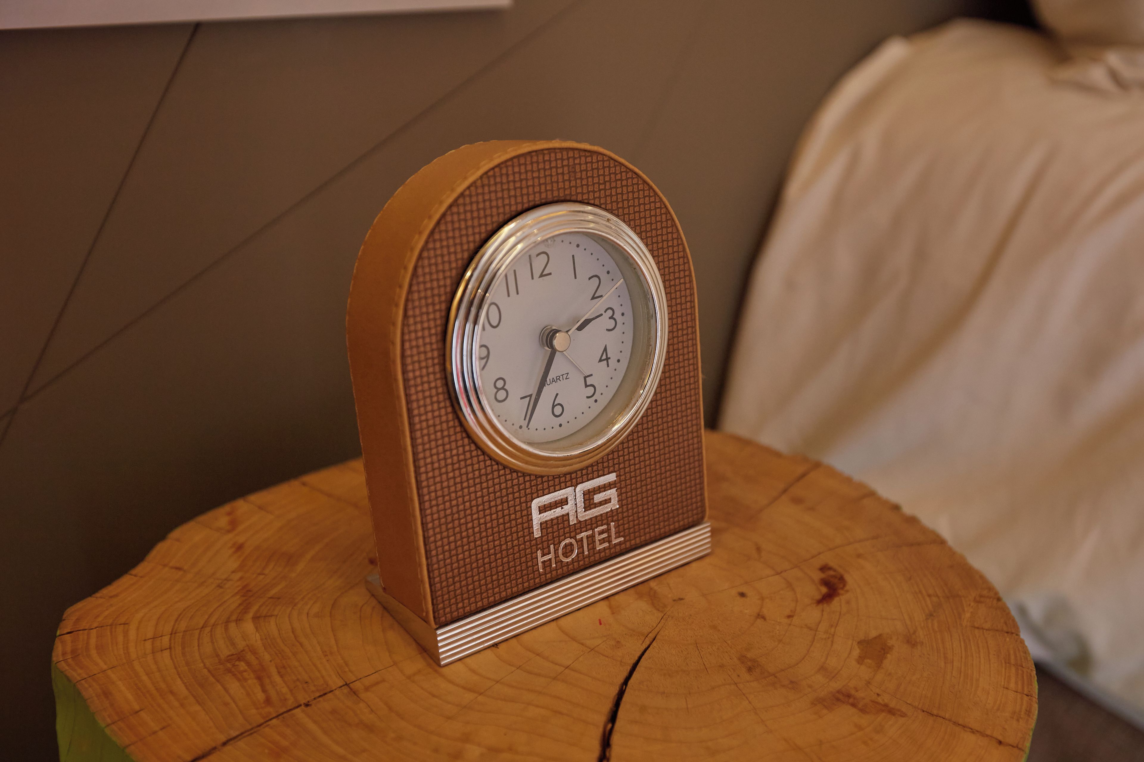 A vintage AG Hotel wall clock with a brown frame and a white face, placed on a wooden round table.