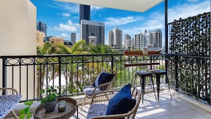 A balcony with wicker furniture, a potted plant, and a view of a cityscape. - `The Ocean Breeze Getaway` by Inn Paradise (Surfers Paradise)