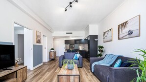 A modern living room with a flat-screen TV, a wooden coffee table, and two grey sofas. - `The Ocean Breeze Getaway` by Inn Paradise (Surfers Paradise)