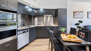 A modern kitchen with stainless steel appliances, a dining area with a wooden table and chairs, and a small potted plant. - `The Ocean Breeze Getaway` by Inn Paradise (Surfers Paradise)