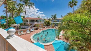 Zona de piscina con vista a un edificio, palmeras y cielo despejado.