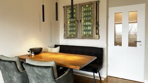A dining area with a wooden table, grey upholstered chairs, a black bench, and a decorative stained glass window above. - Ihr Perfekten Rückzugsort, um die Schönheit des Oberharzes zu Entdecken (Sankt Andreasberg)