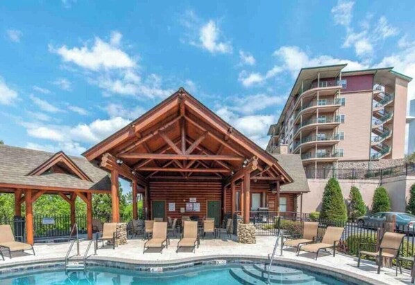 A pool area with lounge chairs and a wooden pavilion.