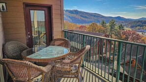 Un balcon agrémenté de meubles en osier et d’une table en verre, offrant une vue sur un paysage montagneux aux couleurs automnales.