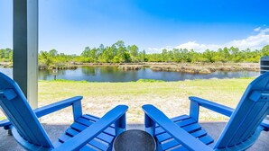 Dos sillas Adirondack azules mirando un río, con árboles y cielo despejado.