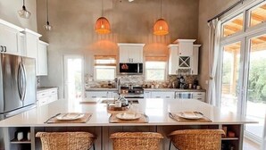 A modern kitchen with a large island, white cabinetry, and three wicker bar stools. - Paradise Cove 3 Bedroom Home (Gregory Town)