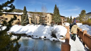 A wooden bridge over a partially frozen river with snow-covered banks and buildings in the background. - On River Trail! Pool, Hot Tub, Elevator! Walk to Festivals, Dining, Shops (Keystone)