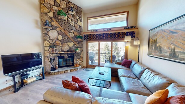 A living room with a stone fireplace, a television, a sofa, and a painting. - On River Trail! Pool, Hot Tub, Elevator! Walk to Festivals, Dining, Shops (Keystone)