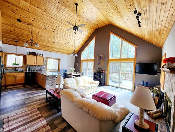 A spacious living area with a high ceiling, wooden beams, a fireplace, and large windows. - Beautiful private Tainter Lake Retreat in Western WI. Sleeps 10 (Menomonie)