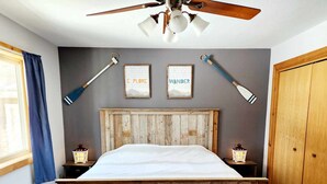 A bedroom with a wooden bed frame, a bench, two wall-mounted lamps, and a ceiling fan.