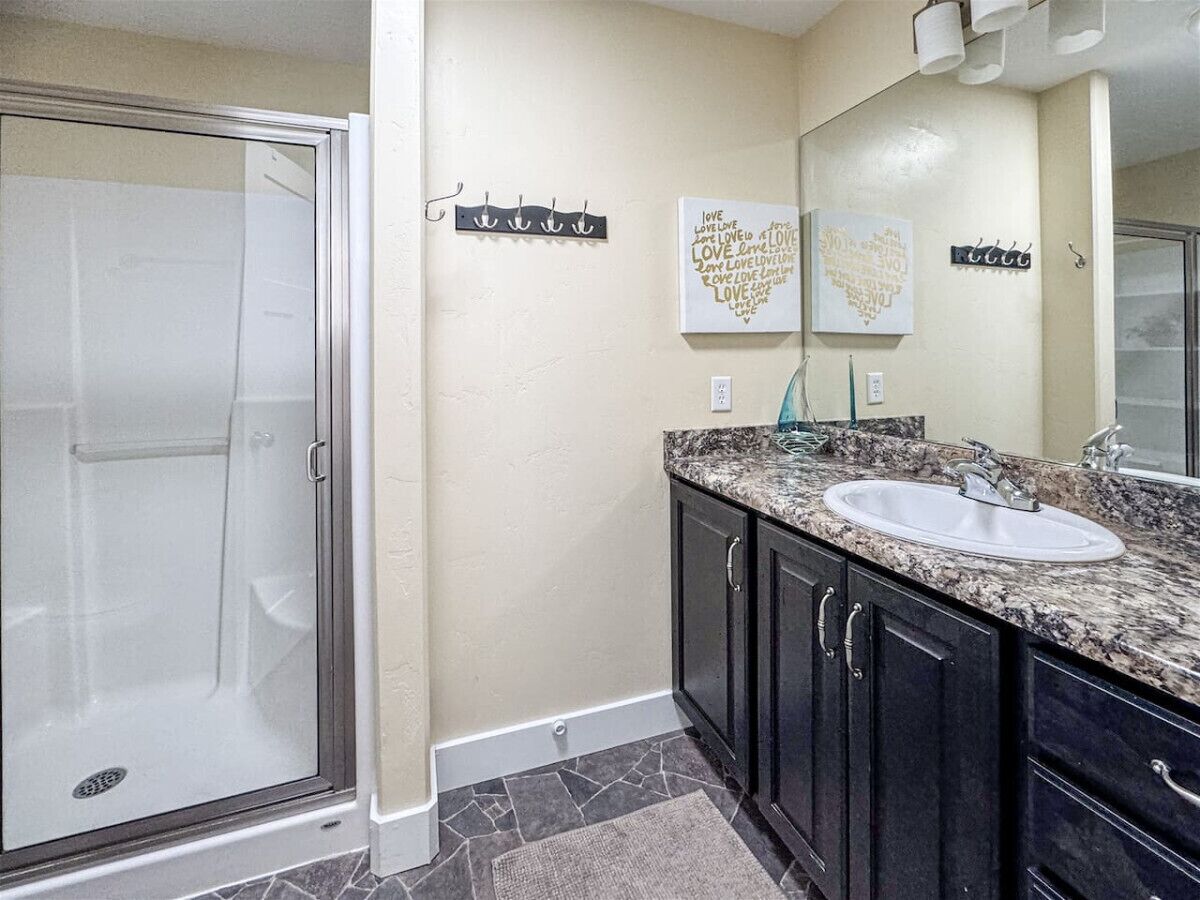 A bathroom with a glass shower enclosure, a sink with a granite countertop, dark cabinets, and two wall-mounted towel racks.