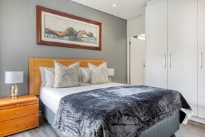 Een slaapkamer met een bed, een nachtkastje, een lamp, een kledingkast en een schilderij aan de muur.
