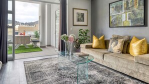 Un soggiorno moderno con un tavolino in vetro, un divano beige con cuscini dorati e un grande quadro astratto appeso al muro.