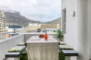 Een balkon met een tafel gedekt voor twee personen, met een fles rosé champagne, twee glazen en een schaal rode druiven.