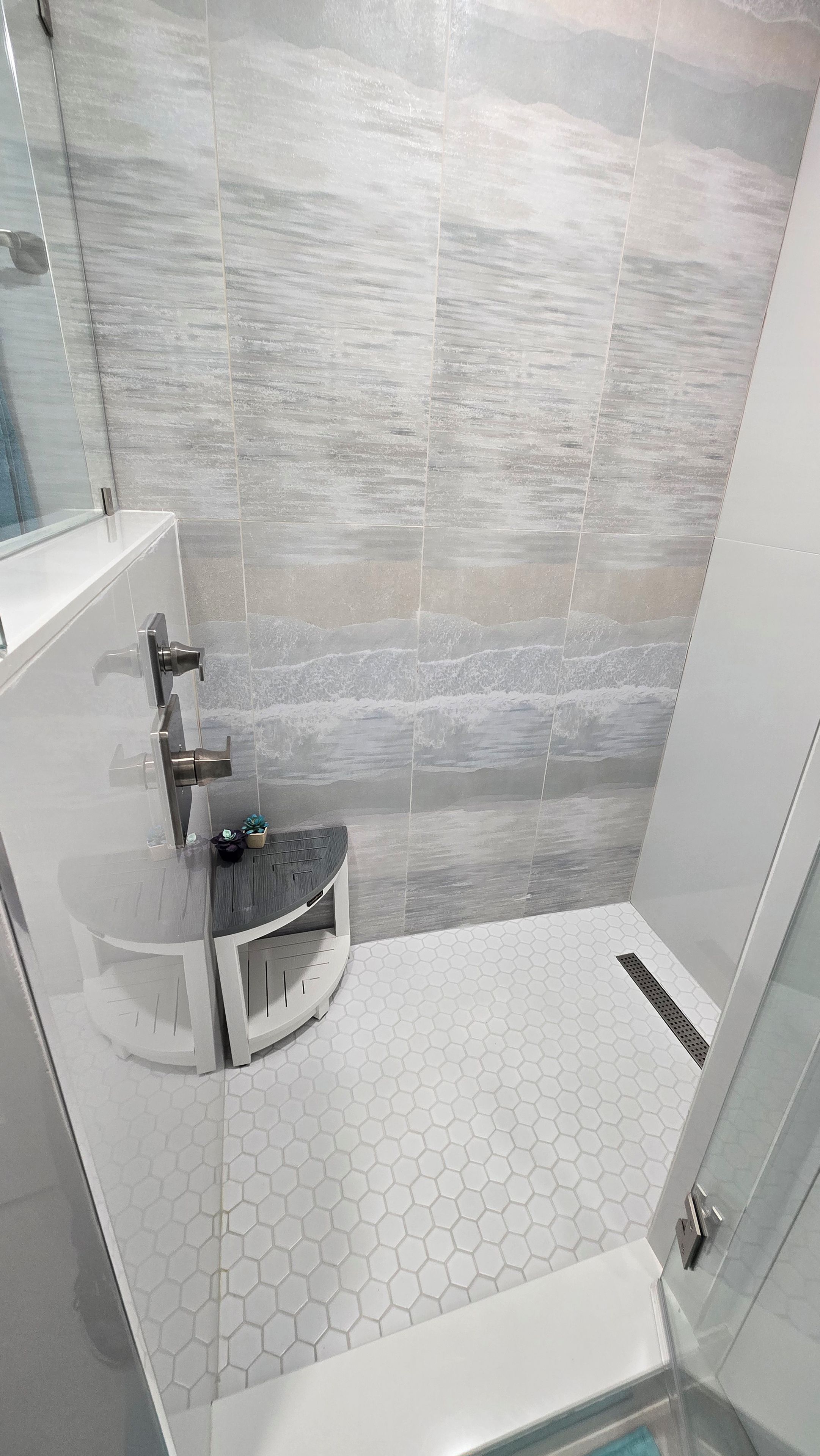 Une salle de bain moderne avec une douche à parois de verre, un lavabo blanc et un sol carrelé avec des motifs hexagonaux.