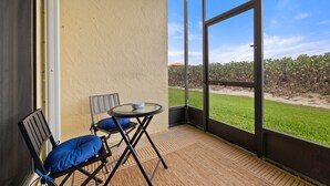Ein Balkon mit Glastür, zwei Stühle mit blauen Kissen und einem kleinen runden Tisch.