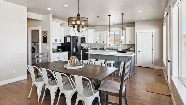 A spacious kitchen with a central island, white cabinetry, and a dining area with a wooden table and white chairs. - Golden Gable Lodge (Sleeps 19) (Fish Haven)