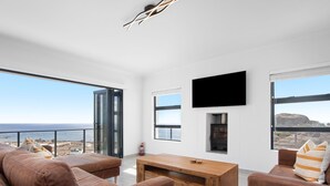 Una sala de estar moderna con un ventanal grande que da al mar, un televisor de pantalla plana en la pared y una mesa de centro de madera.