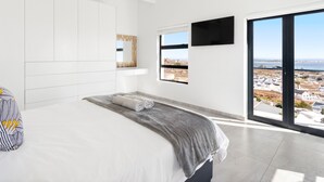 Un dormitorio moderno con una cama grande, vista de la ciudad a través de una puerta corredera y un techo con vigas a la vista.