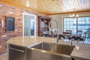 A kitchen with a brick wall, a stainless steel sink, and a wooden dining table with chairs.