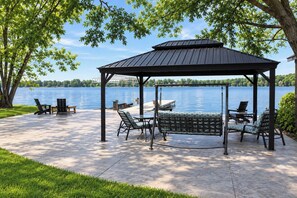 A gazebo with a swing, outdoor seating, and a view of a lake.