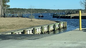 Een park aan het water met een betonnen pad, houten steigers en een klein bootje.
