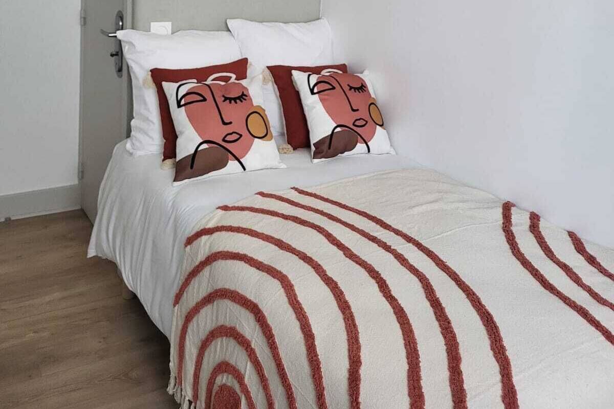 Une chambre à coucher avec un lit, des oreillers, une couverture, une porte et un mur orné d’un cadre contenant une citation.
