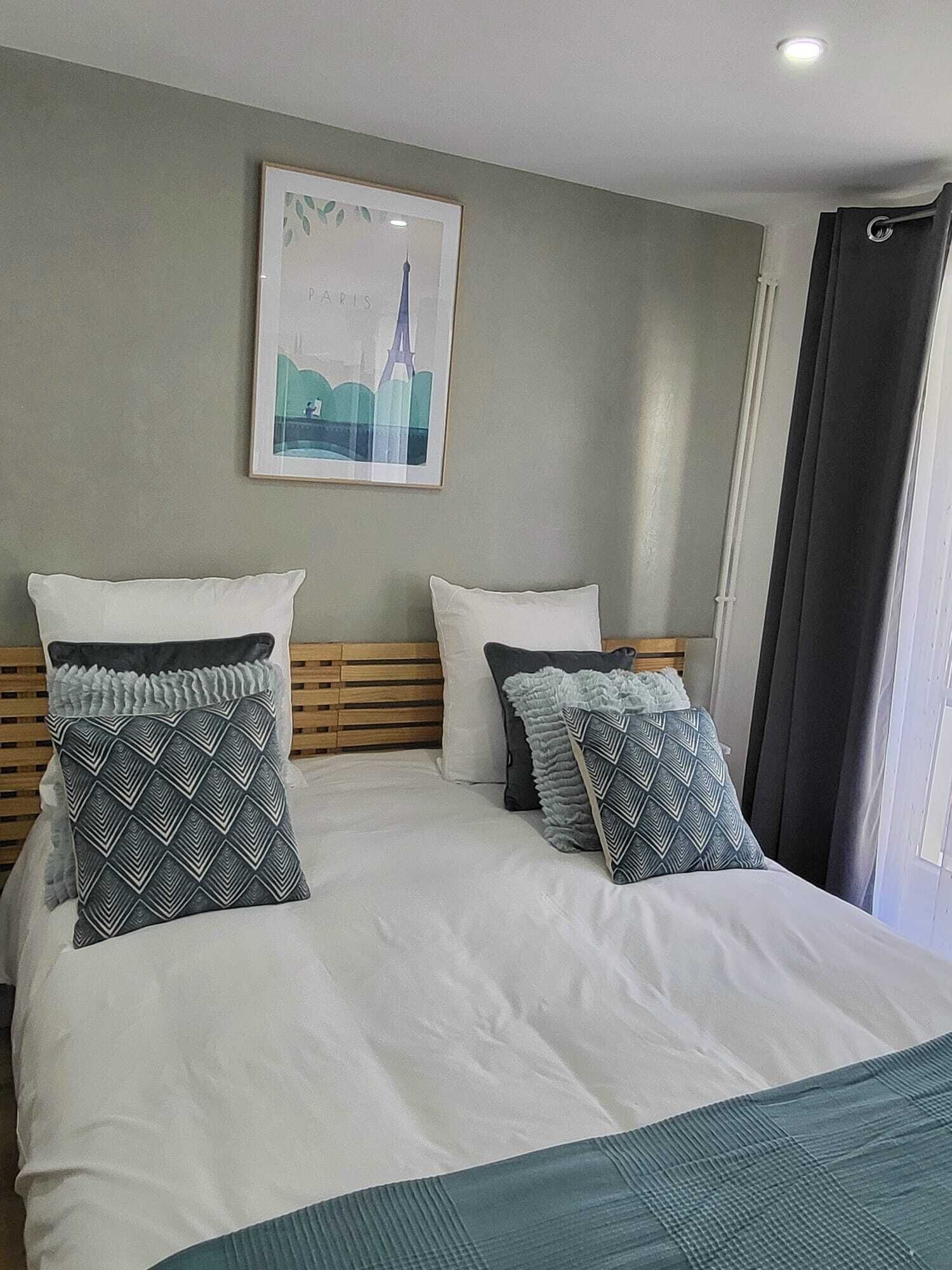 A hotel room with a large bed, two pillows, a framed picture of the Eiffel Tower, and a window with curtains.