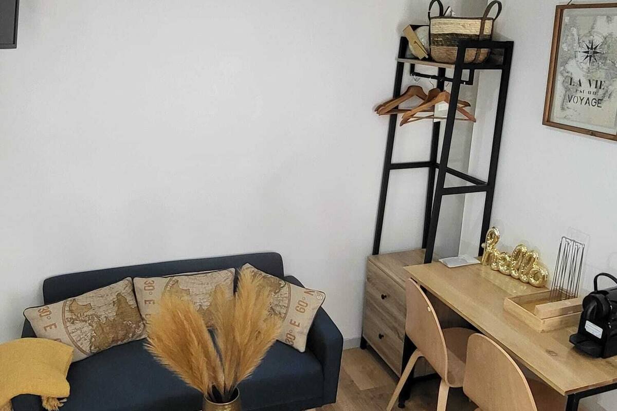 Un salon moderne avec un canapé bleu foncé, une table basse en bois, un bureau en bois avec une chaise, une échelle en métal noir et une carte encadrée accrochée au mur.