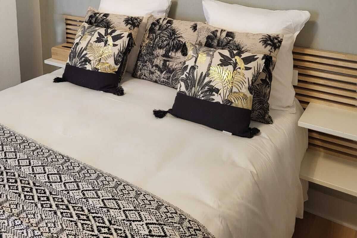 Un lit avec une couette blanche, deux oreillers à motifs tropicaux et une carte accrochée au mur.