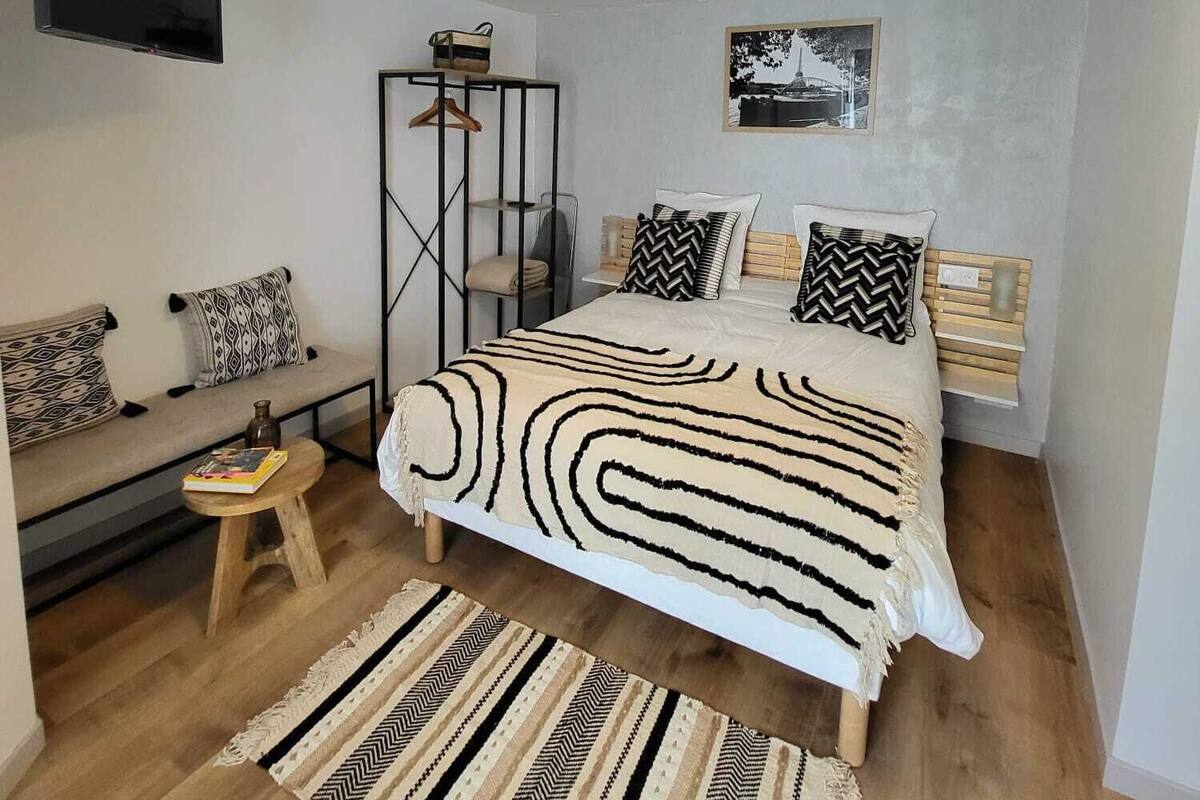 Une chambre moderne avec un lit, une télévision, un luminaire suspendu, un plancher en bois et un banc.
