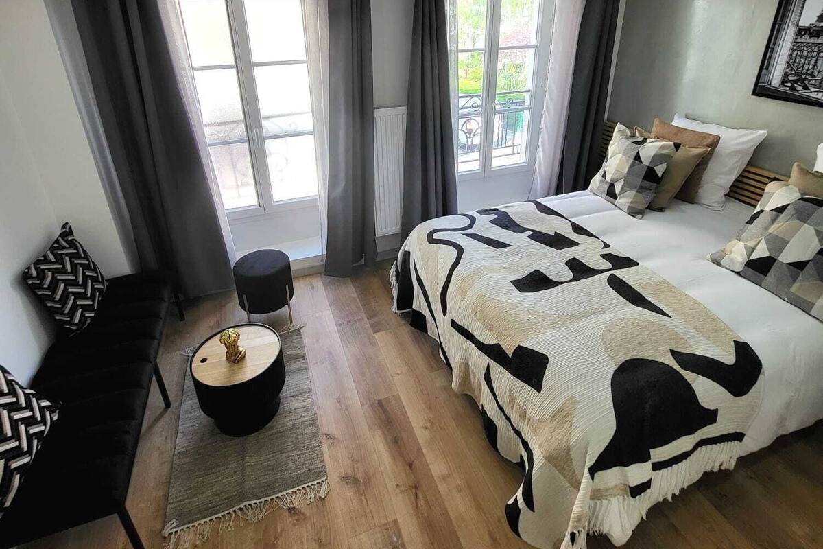 Une chambre moderne avec un grand lit, une petite table ronde, un canapé et une vue sur l’extérieur grâce à de grandes fenêtres.
