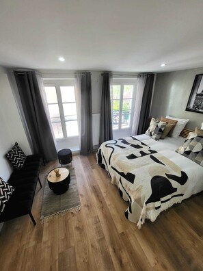 Un dormitorio moderno con una cama grande, una mesita redonda pequeña, un sofá y vistas al exterior a través de ventanas amplias.