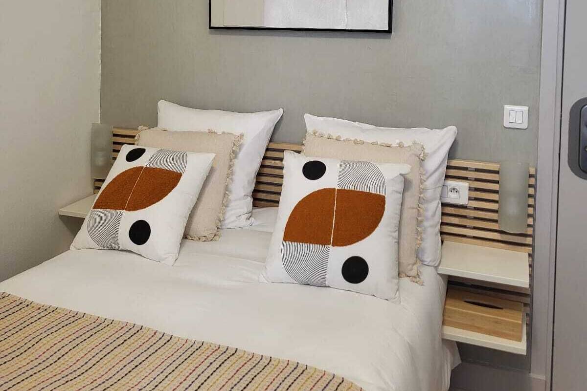 Une chambre à coucher comprenant un lit, deux oreillers, une table de chevet et une œuvre d’art accrochée au mur.