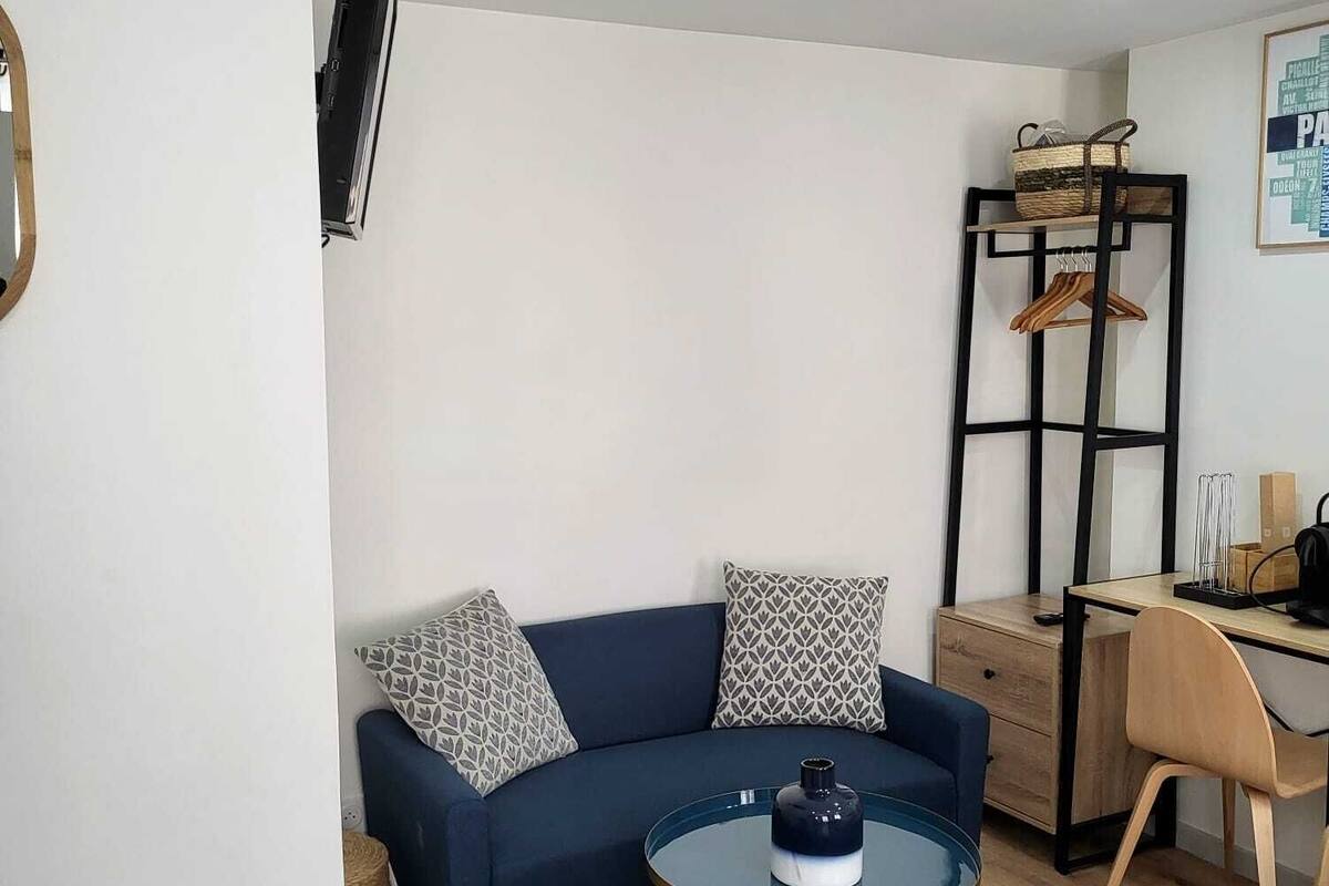 Un salon moderne comprenant un canapé, une table basse ronde, un téléviseur fixé au mur, un bureau avec une chaise et une petite poubelle.