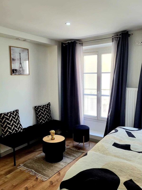Una habitación moderna con sofá, una mesita redonda, cama y ventana con cortinas.