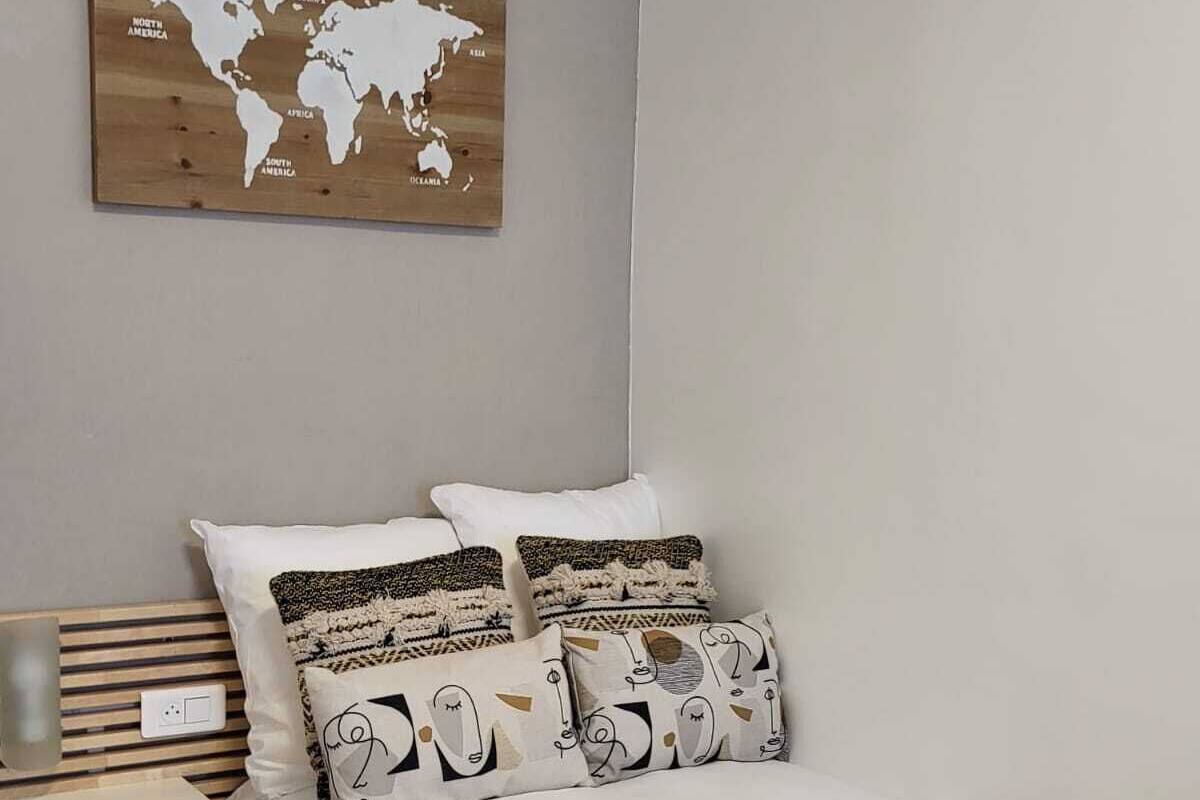 Une chambre à coucher avec un lit, des oreillers, une tête de lit en bois, une table de chevet et une carte du monde accrochée au mur.