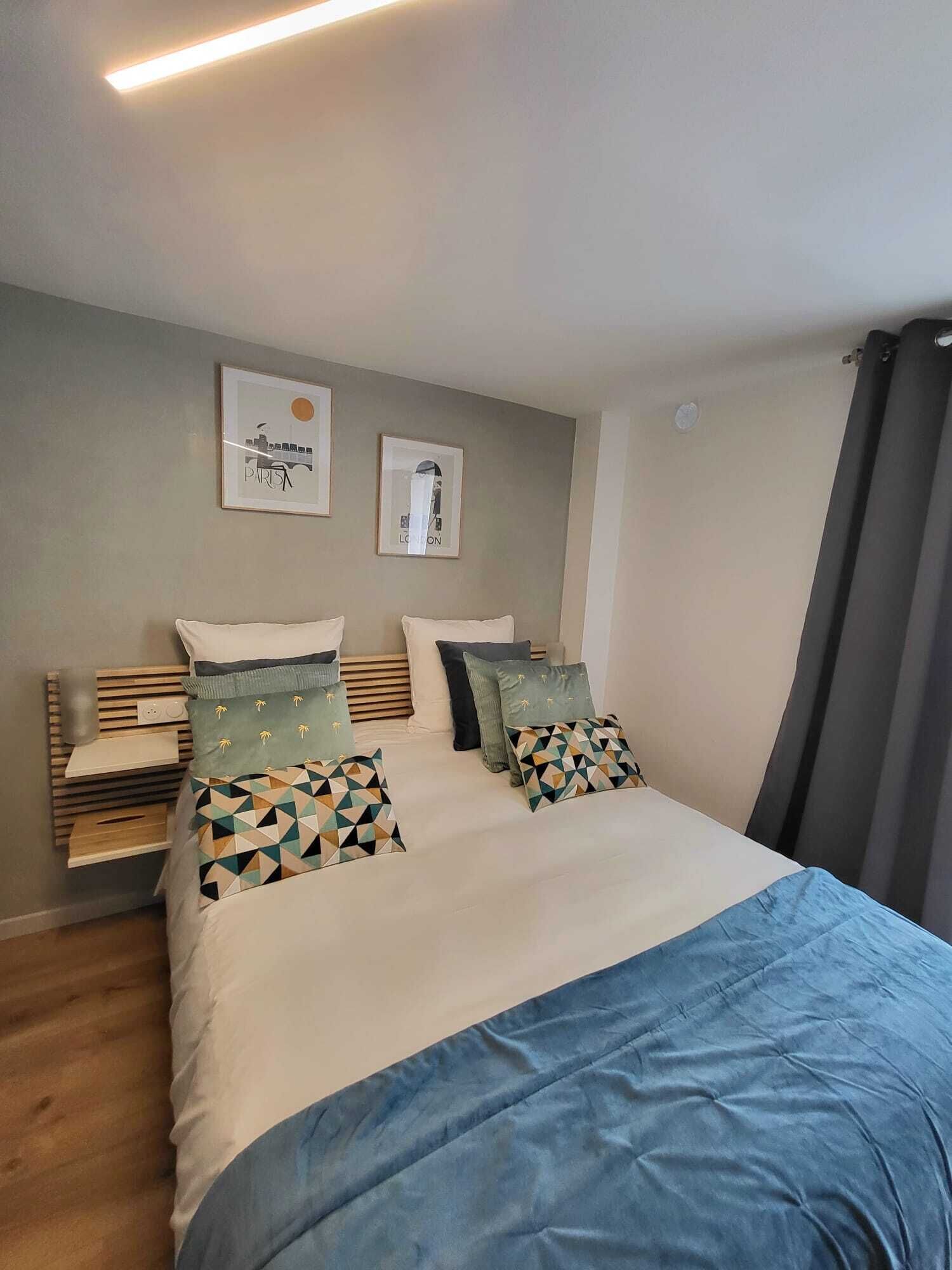 Un dormitorio con cama, almohadas, una mesita de noche y decoración en la pared.