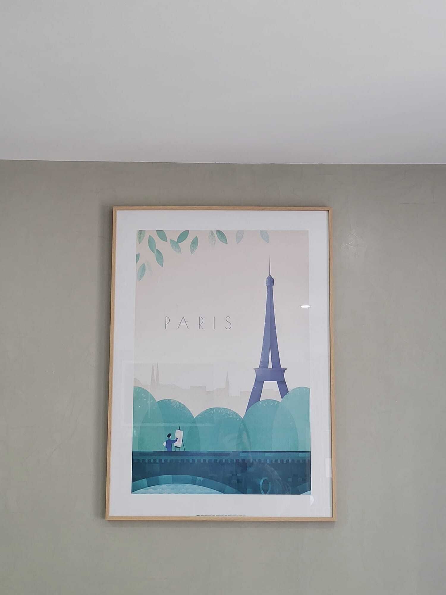 A framed artwork of the Eiffel Tower with the word "PARIS" above it, set against a plain wall.