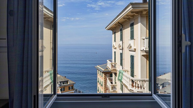 A view from a window overlooking a coastal street with buildings and the sea.