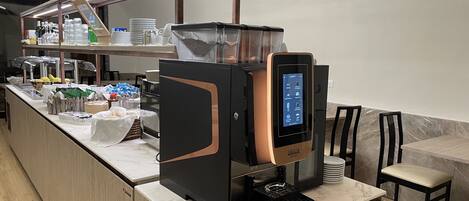 A self-service coffee station with a touchscreen interface, a coffee machine, and a variety of coffee pods and milk options.