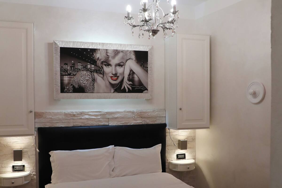 A bedroom with a bed, a chandelier, a wall-mounted picture, and bedside lamps.