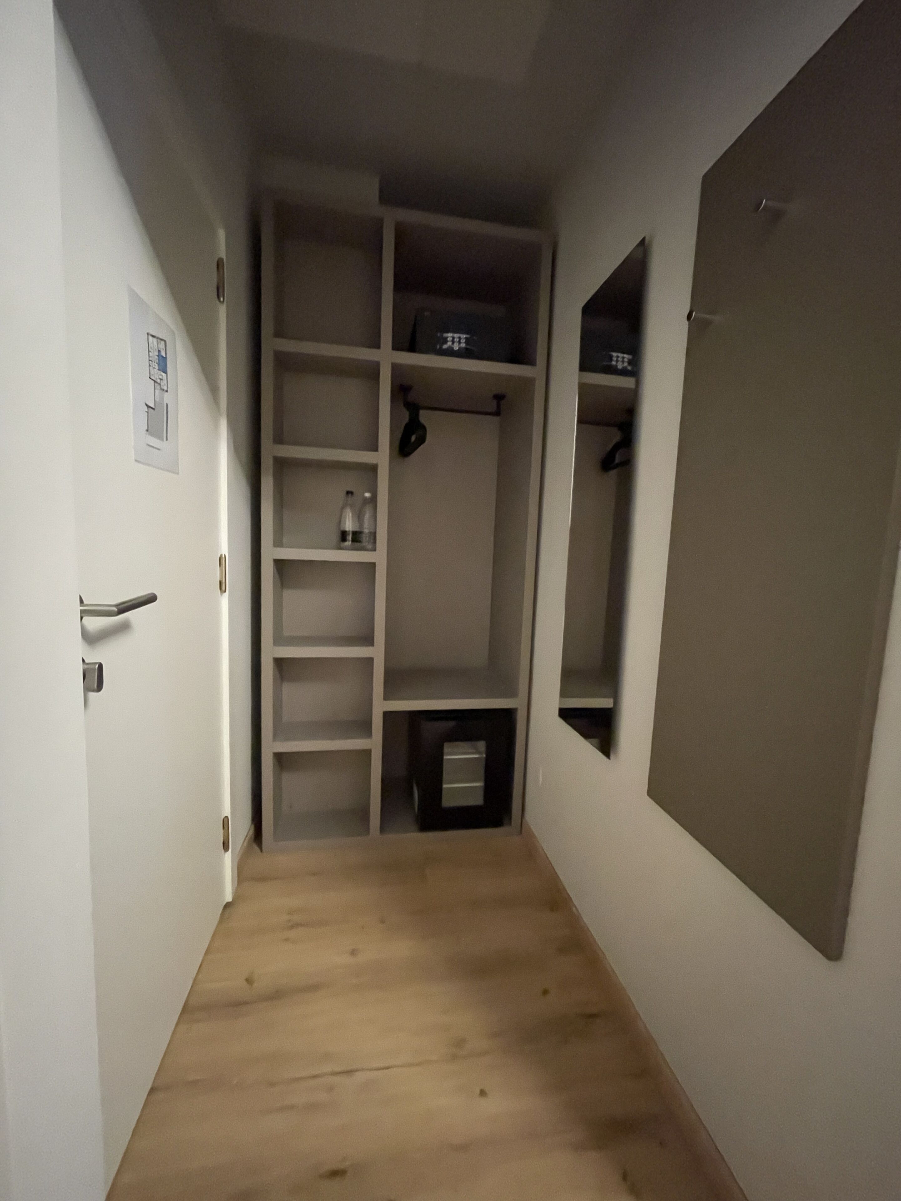 Un couloir étroit, doté d’un plancher en bois, mène à un placard équipé d’étagères et d’une tringle pour suspendre les vêtements.